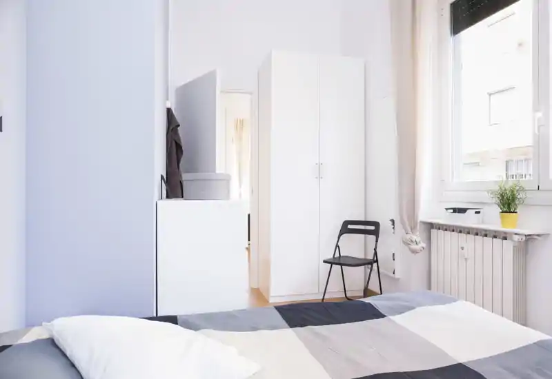 Dormitorio luminoso y minimalista con cama bien hecha, armario blanco y ventana que aporta luz natural — ideal para el anuncio.