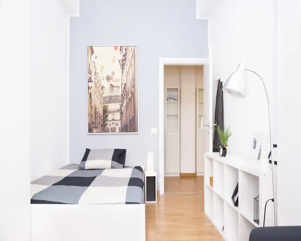 Camera da letto luminosa e ordinata con letto matrimoniale, scaffalatura moderna e arredi essenziali; perfetta per annunci che promuovono design minimale e luce naturale.