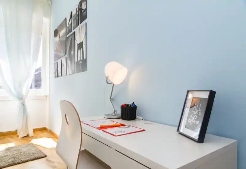 Area studio luminosa e minimale con scrivania bianca, lampada e sedia vicino alla finestra — tocchi decorativi ordinati e luce naturale adatti per lavorare concentrati.