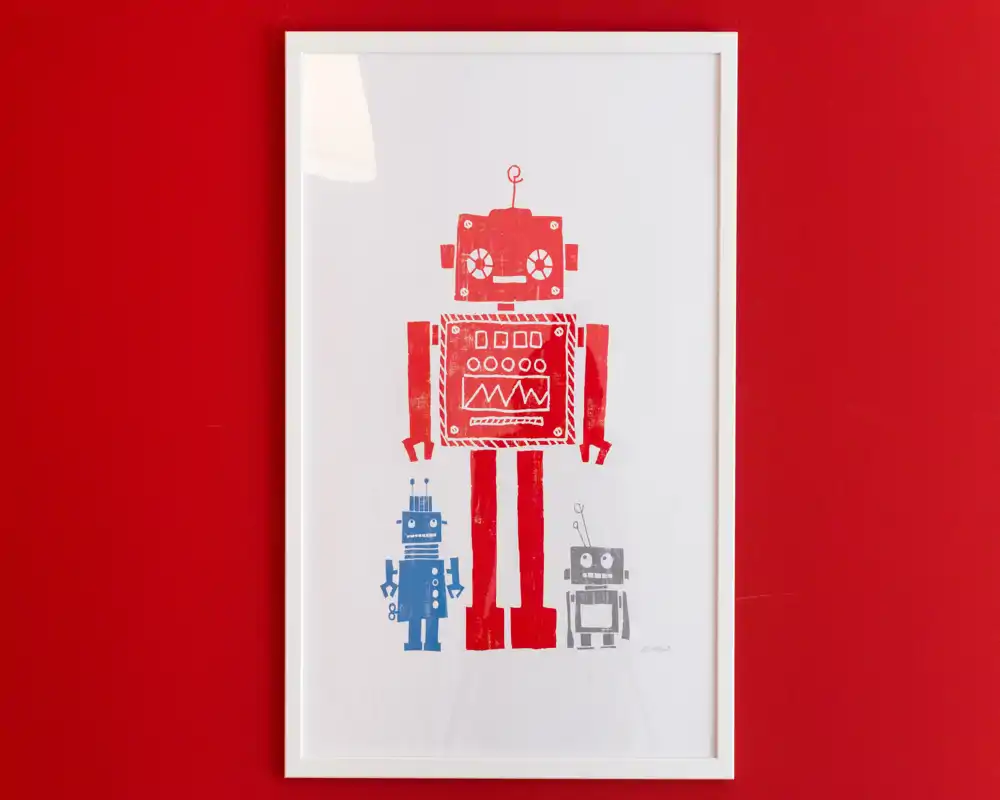 Primer plano de una lámina de robots enmarcada sobre una pared roja intensa; decoración indicada para una habitación infantil o un espacio de vida divertido.