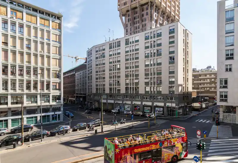 Vista urbana luminosa con un incrocio cittadino, edifici di media altezza e un autobus scoperto turistico in primo piano.