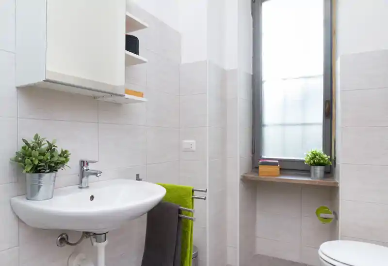 Bagno moderno e luminoso con lavabo a parete, portasciugamani e finestra in vetro satinato che diffonde luce naturale.