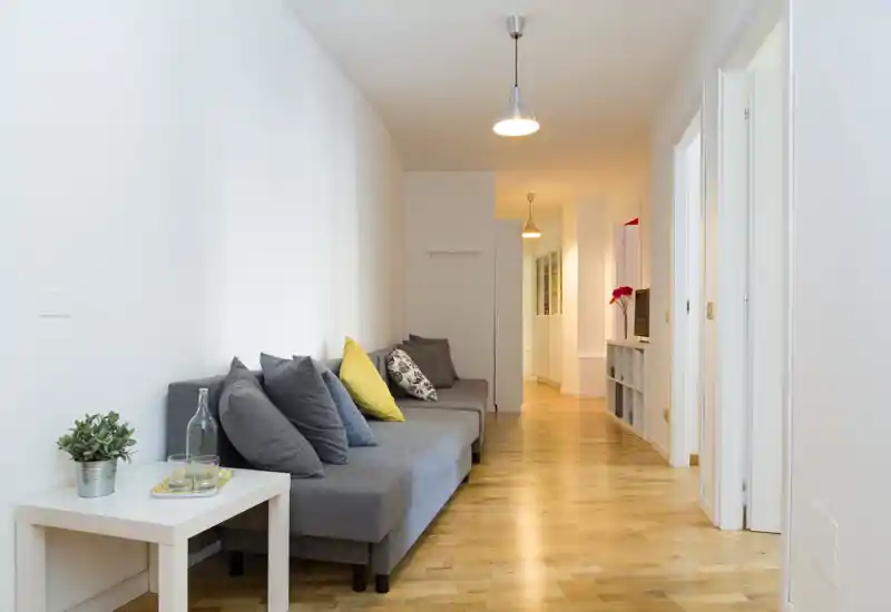 Zona giorno luminosa e moderna con un lungo divano grigio, cuscini decorativi e pavimento in legno caldo — corridoio living ordinato e accogliente.