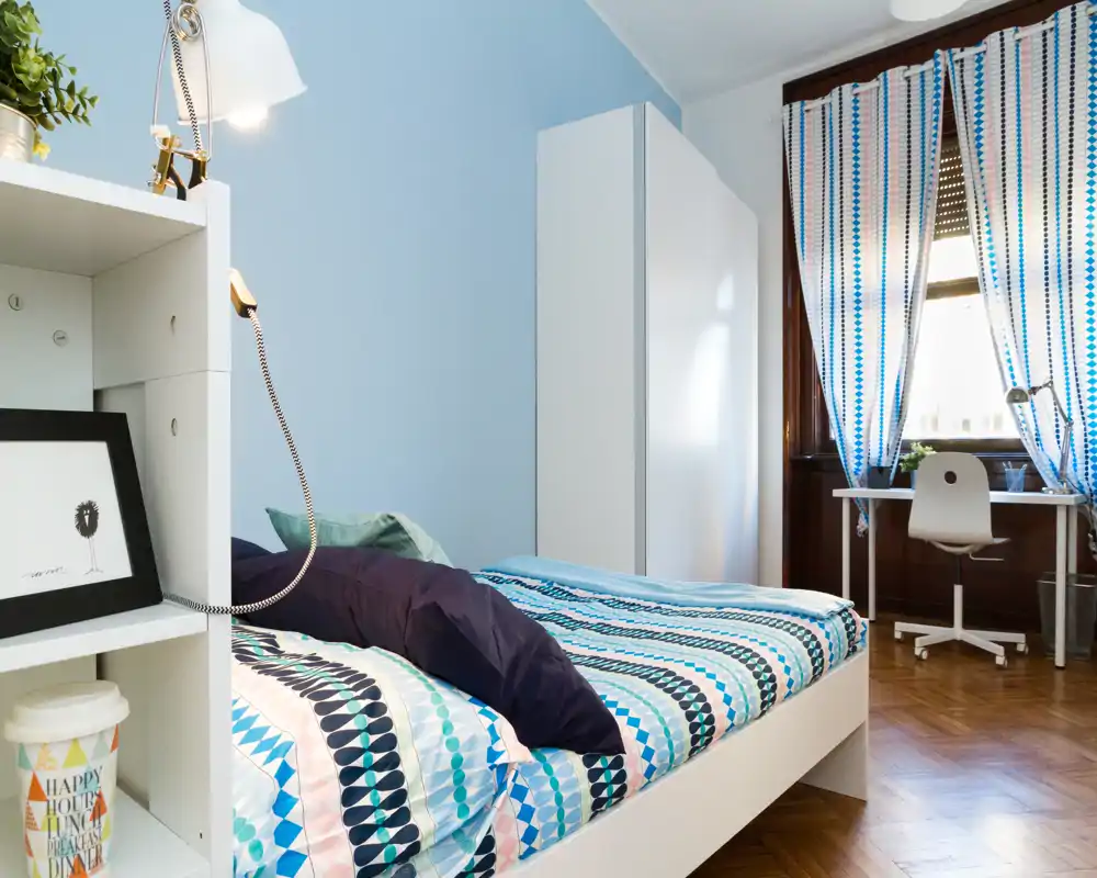 Dormitorio luminoso y bien decorado con cama estampada, almohadas cómodas y escritorio junto a la ventana — ideal para una estancia cómoda o para estudiantes.