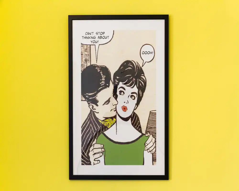 Una stampa pop-art incorniciata appesa a una parete giallo vivace; la foto mostra l'opera d'arte murale più che gli arredi di una stanza specifica.