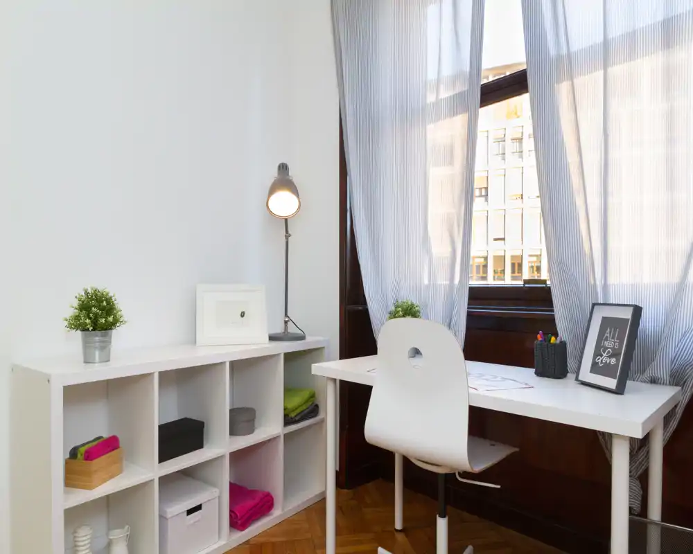 Angolo lavoro luminoso e ordinato con scrivania bianca, sedia ergonomica e scaffalatura, illuminato da una grande finestra con luce naturale morbida.