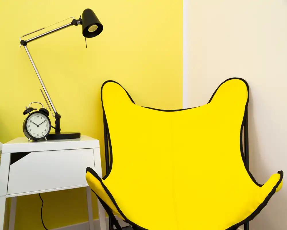 Angolo conversazione luminoso e moderno con poltrona gialla vivace, tavolino, lampada e sveglia: perfetto come angolo lettura o relax.
