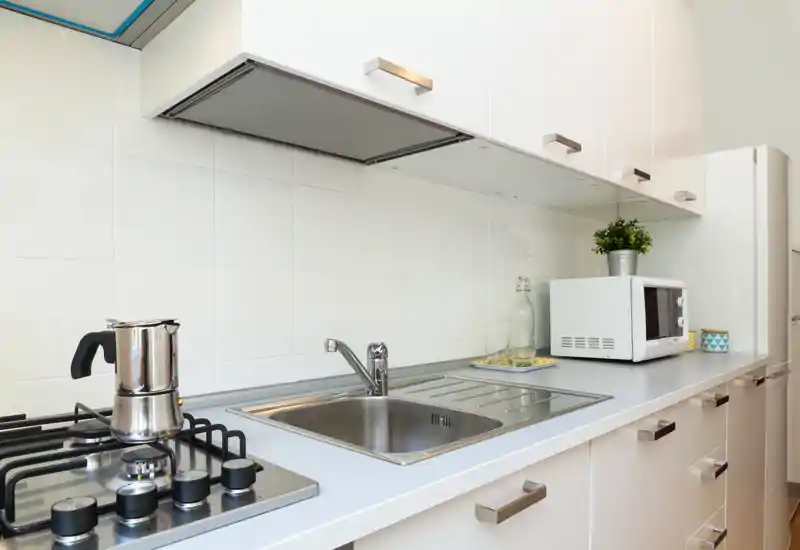 Cucina moderna e luminosa con lavello in acciaio, piano cottura a gas e microonde; mobili bianchi minimal creano un’area cucina pulita e funzionale.