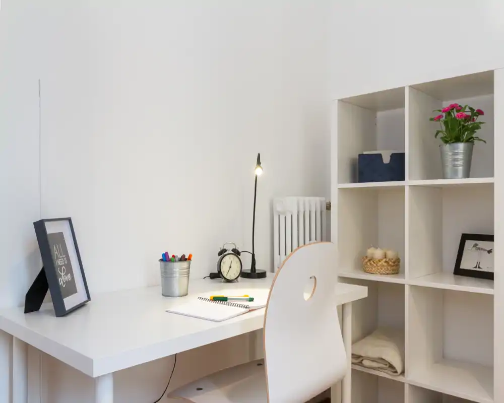 Coin bureau lumineux et minimaliste avec bureau blanc, chaise, lampe et étagères — espace de travail rangé idéal pour la concentration.