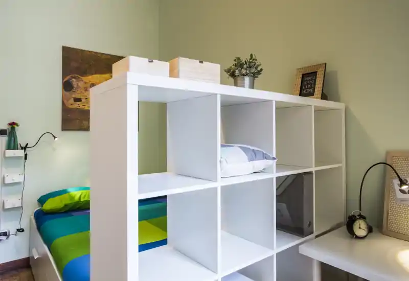 Bright, modern bedroom with a colorful bed partially visible behind a white cube shelving unit and tasteful decorative accents.