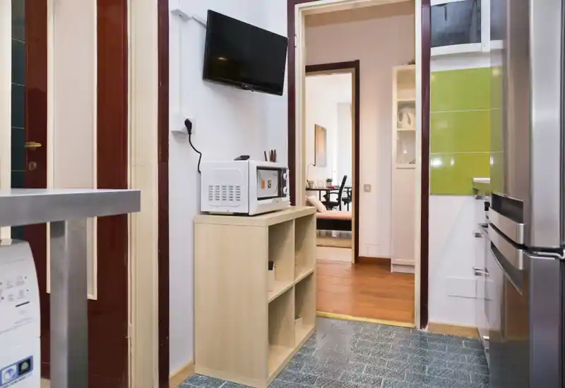 Compact kitchen area with refrigerator, microwave and shelving; view through to an adjacent living space. Well-organized layout suitable for short-term rental listings.