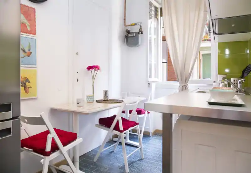 Compact, bright kitchen with a small dining nook, white cabinetry, and red seat cushions creating a cozy atmosphere.