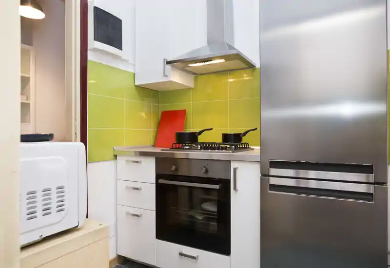 Compact modern kitchen with stainless-steel fridge, built-in oven and gas hob against a green-tiled backsplash — bright, tidy and well-equipped for short stays.