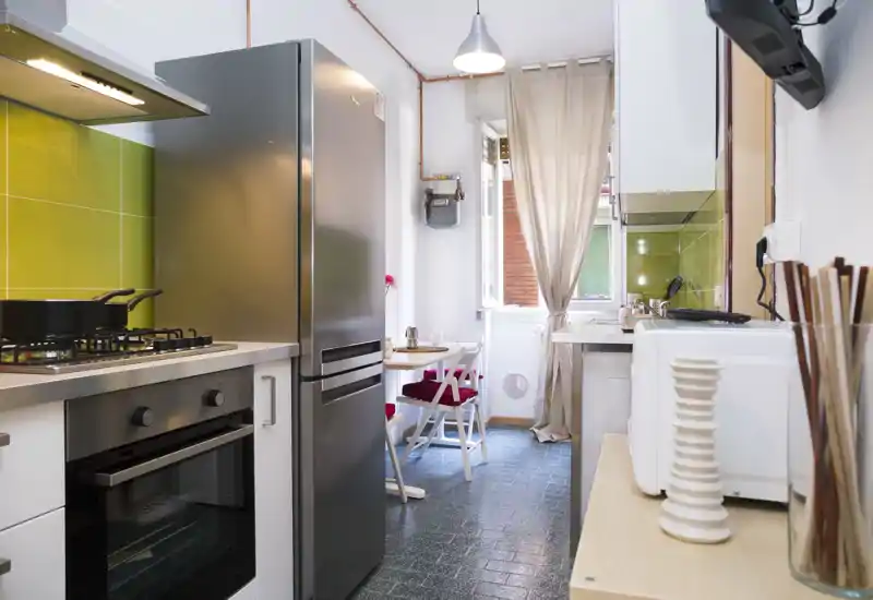 Compact modern kitchen with stainless appliances, a gas hob, and a small dining table by a bright window — ideal for cozy urban living.