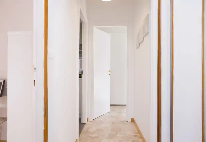 Bright, tidy corridor with white doors and tiled floor; ideal as an apartment entrance or hallway photo highlighting doorways and flow between rooms.