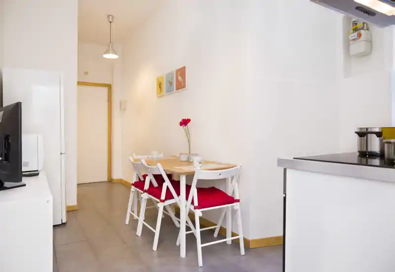 Small dining nook with a wooden table and four white chairs with red cushions, bright walls and simple decorative accents, adjacent to the kitchen counter.