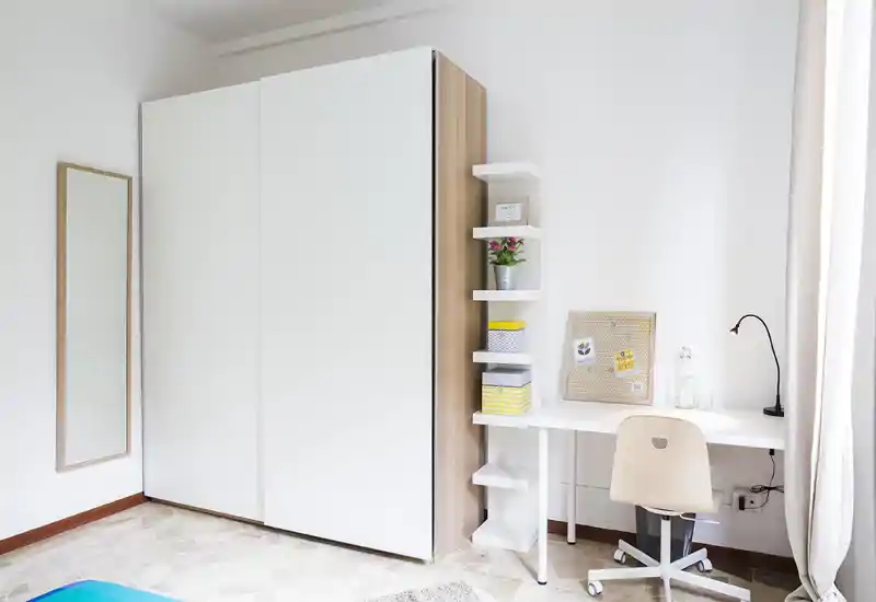 Bright, minimal bedroom corner with a large white wardrobe, compact desk and a simple chair — ideal for a tidy work-and-sleep setup.