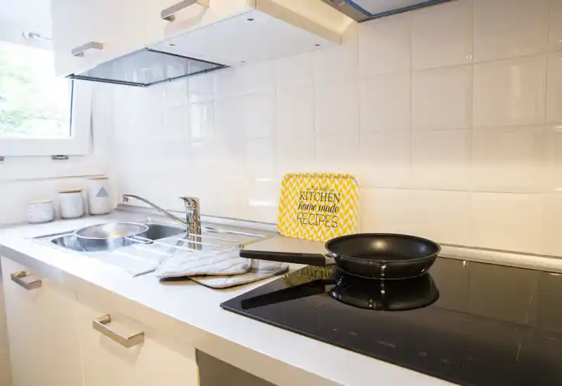 Piano di lavoro cucina moderno e luminoso con lavello, piano a induzione e padella; allestito con cura con barattoli e una tavoletta decorativa delle ricette.
