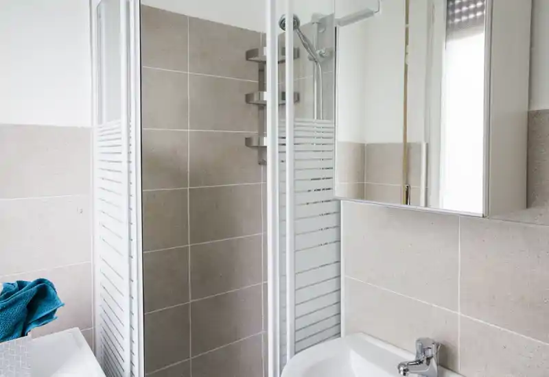 Bagno moderno e pulito con pareti piastrellate, lavabo angolare e box doccia in vetro, ben illuminato e dallo stile minimal.