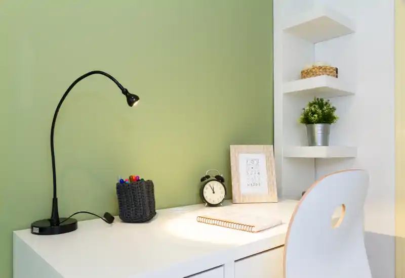 Bright, tidy desk corner with a modern lamp, clock, notebook and small decorative plant — a compact home office or study nook.