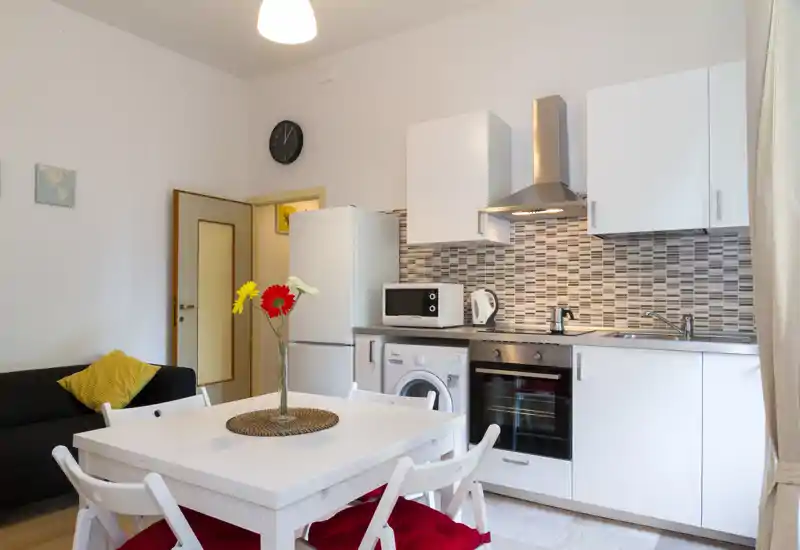 Bright, modern open-plan living area with a compact white kitchenette, dining table for four and a small sofa — ideal for a cozy city apartment.