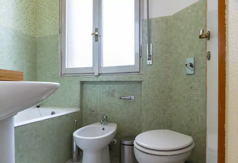 Compact bathroom with bathtub, bidet and toilet, tiled walls in pale green and a frosted window providing natural light.
