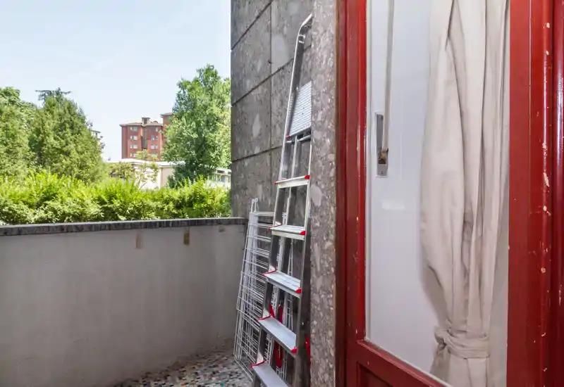 Small private balcony with tiled floor, a folding ladder and a drying rack; leafy views and good daylight make it suitable for fresh-air breaks.