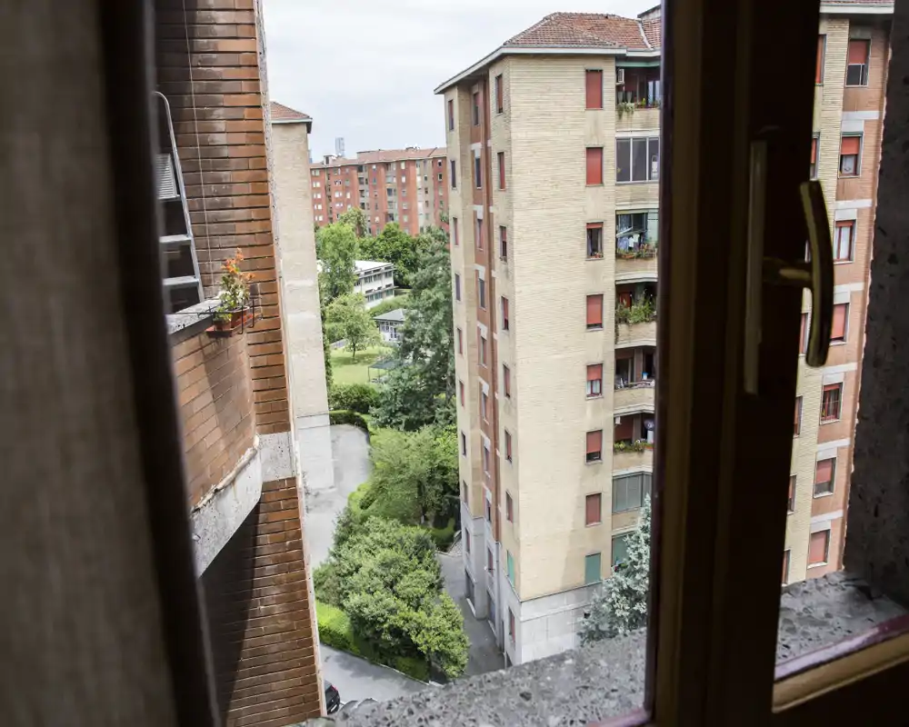 View from a window/balcony overlooking neighboring apartment buildings and a small courtyard with trees; suitable to show the outdoor view and surroundings.