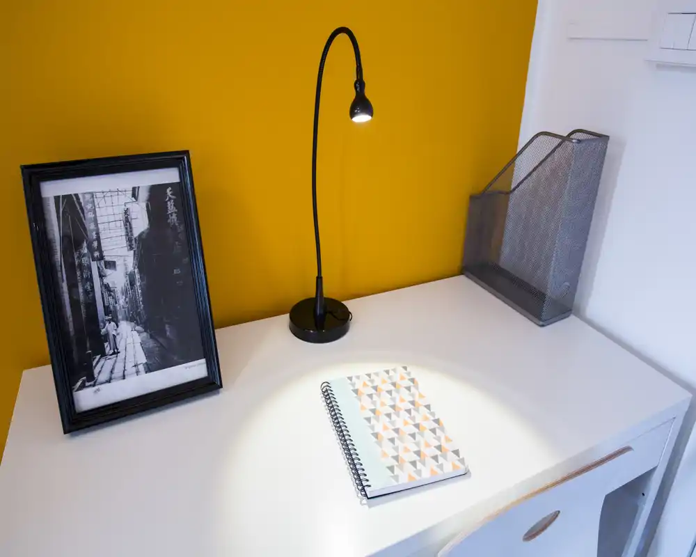 Bright, modern desk corner with a white tabletop, a flexible black desk lamp, framed black-and-white photo and a patterned spiral notebook — ideal for a compact workspace.