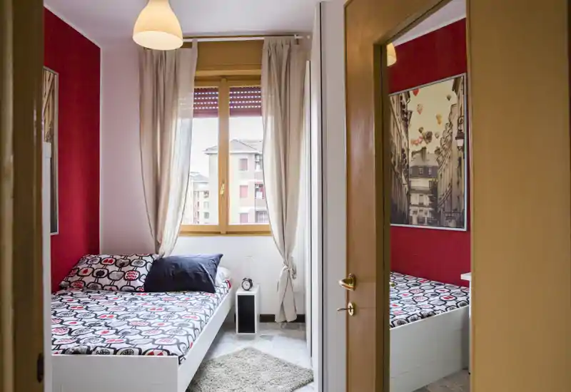 Chambre simple lumineuse et accueillante avec linge de lit à motifs, table de chevet et grande fenêtre aux rideaux légers apportant une belle lumière naturelle.