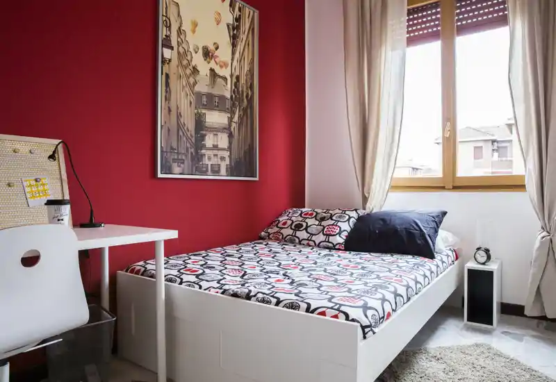 Chambre simple lumineuse et accueillante avec literie à motifs, cadre de lit blanc, bureau et grande fenêtre apportant une belle lumière naturelle — idéale pour un étudiant ou une personne seule.