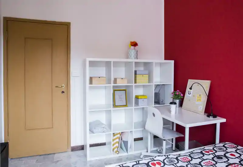 Coin chambre compact avec lit simple visible, étagère blanche et petit bureau avec chaise — lumineux, soigné et décoré avec goût pour un espace fonctionnel.