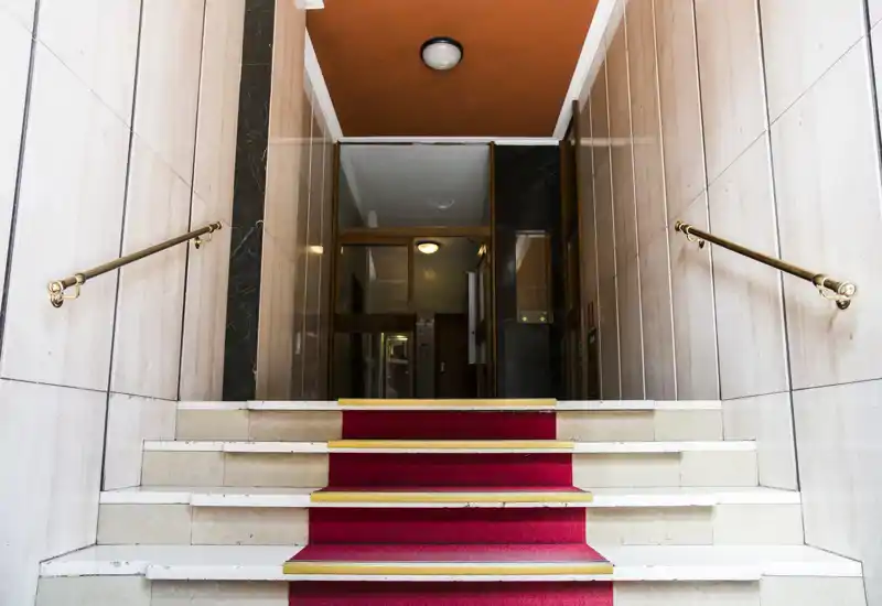 Symmetrical building entrance with a short flight of carpeted steps, brass handrails and a well-lit hallway beyond — ideal for highlighting access and curb appeal.