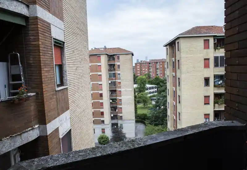 Small urban balcony view overlooking neighboring apartment blocks and a courtyard with trees; ideal to advertise as a balcony with city outlook.