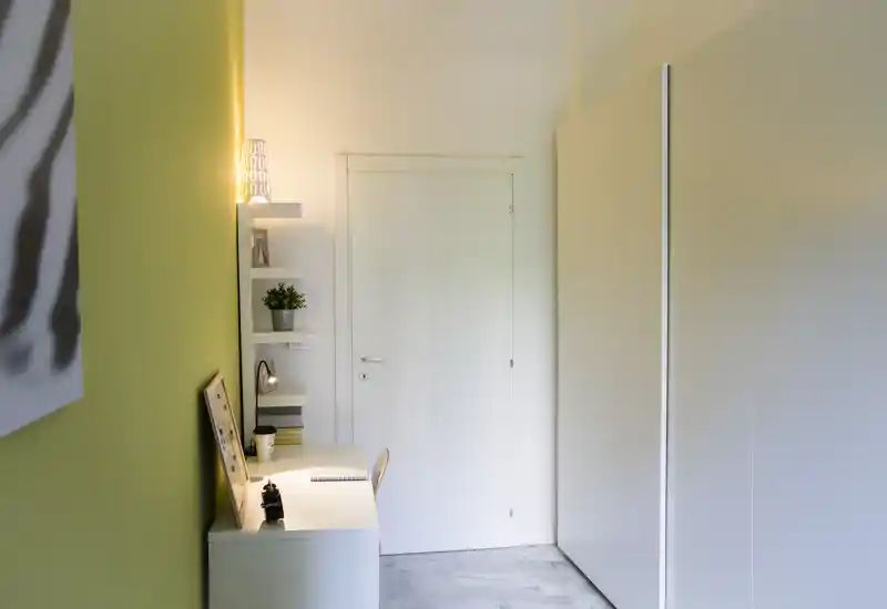 Ingresso/corridoio compatto con una piccola scrivania, mensole a parete e armadio; stile minimal, luminoso e funzionale.