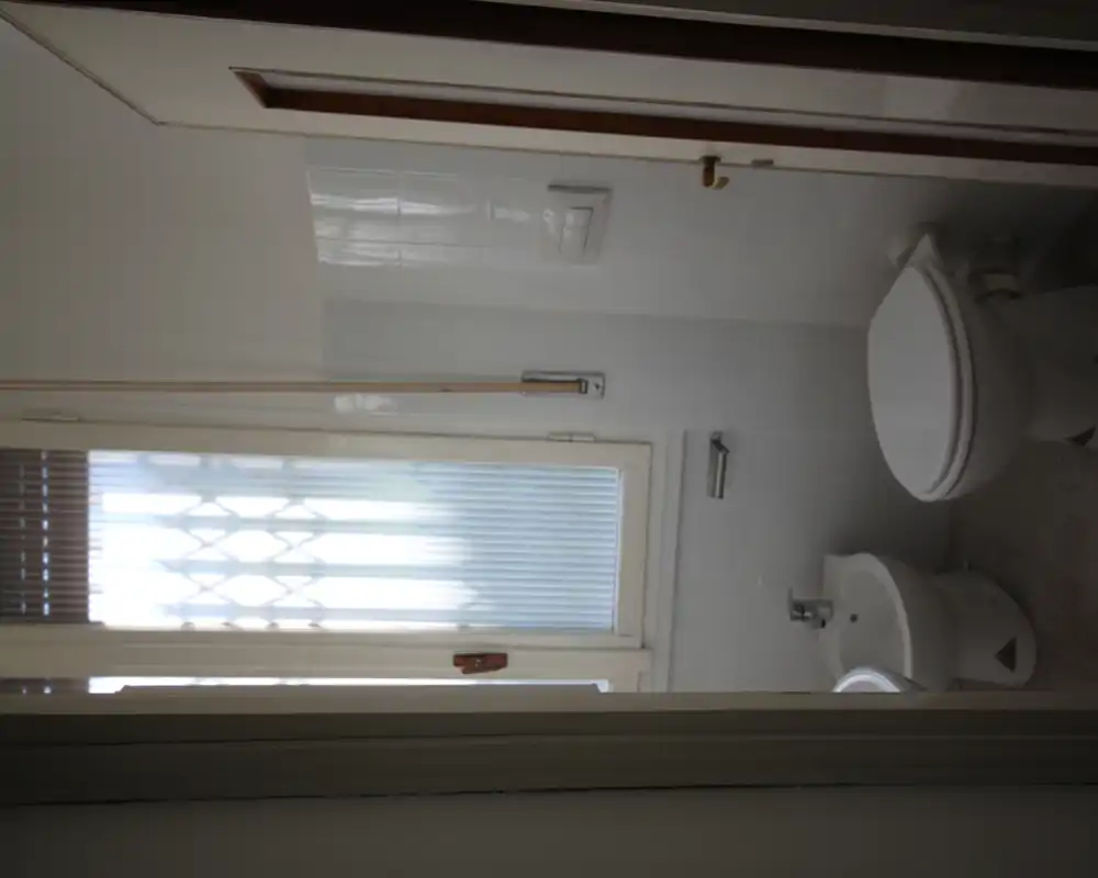 Bagno compatto con WC e bidet accanto a una finestra con vetro satinato, piastrelle bianche e luce naturale. Ideale per un appartamento piccolo.