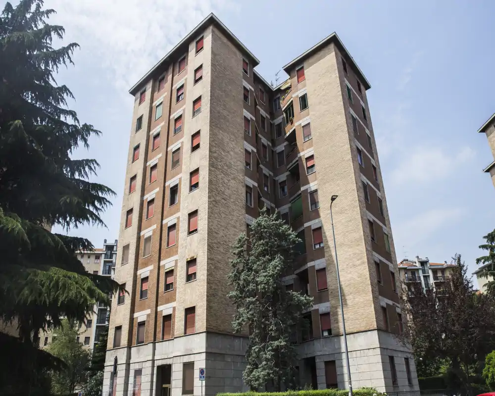 Vista esterna di un edificio residenziale in mattoni di media altezza con più piani, circondato da alberi e cielo sereno — ideale come foto dell'esterno della proprietà.