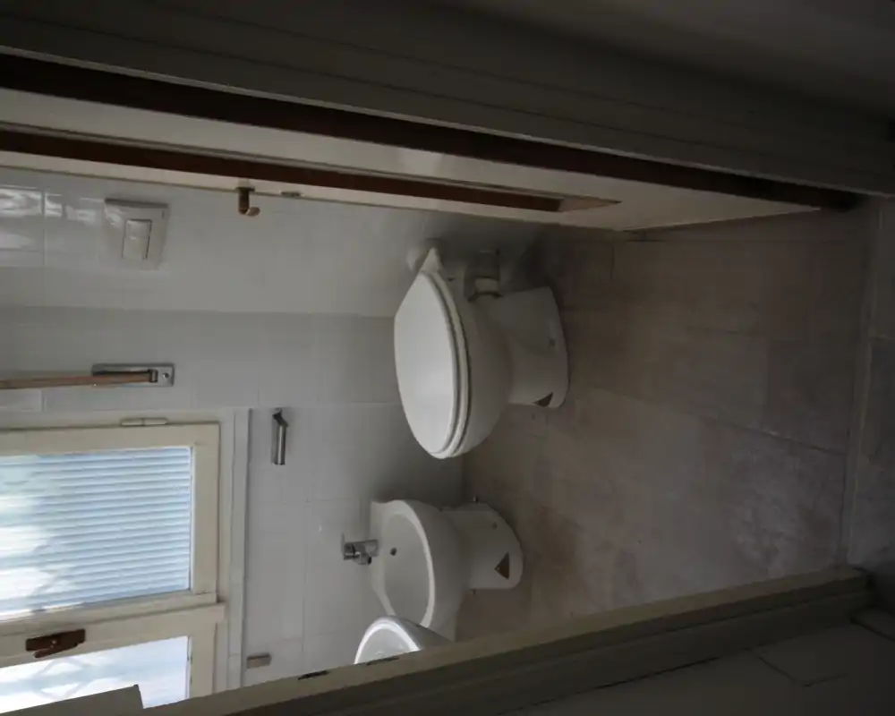 Piccolo bagno con WC, bidet e lavabo visibili, piastrelle neutre e finestra satinata che diffonde luce naturale.