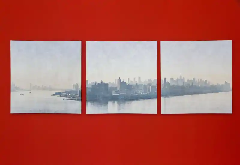 Un trittico raffigurante un paesaggio urbano esposto su una parete rossa. I tre pannelli mostrano uno skyline nebbioso sul mare calmo, utilizzato come elemento decorativo.