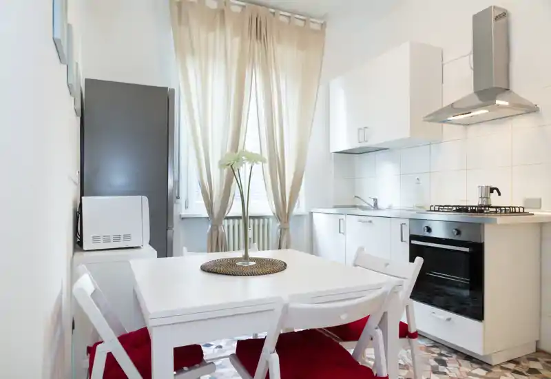 Cucina moderna e luminosa con piccolo tavolo da pranzo, mobili bianchi, piano cottura a gas e forno — perfetta per appartamenti urbani compatti.