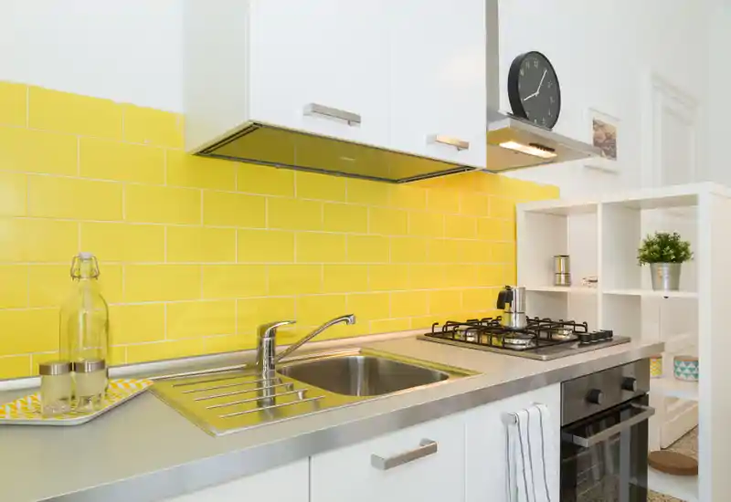 Compact modern kitchen with a stainless-steel sink, gas hob and bright yellow tiled backsplash creating a fresh, stylish look.