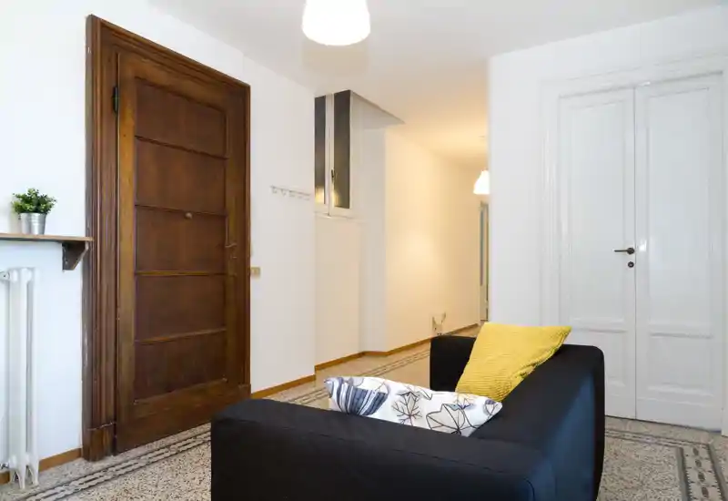 Bright, tidy living area with a dark sofa accented by patterned and yellow cushions, tiled decorative floor and clean white walls — ideal for a cozy entrance-lounge setup.