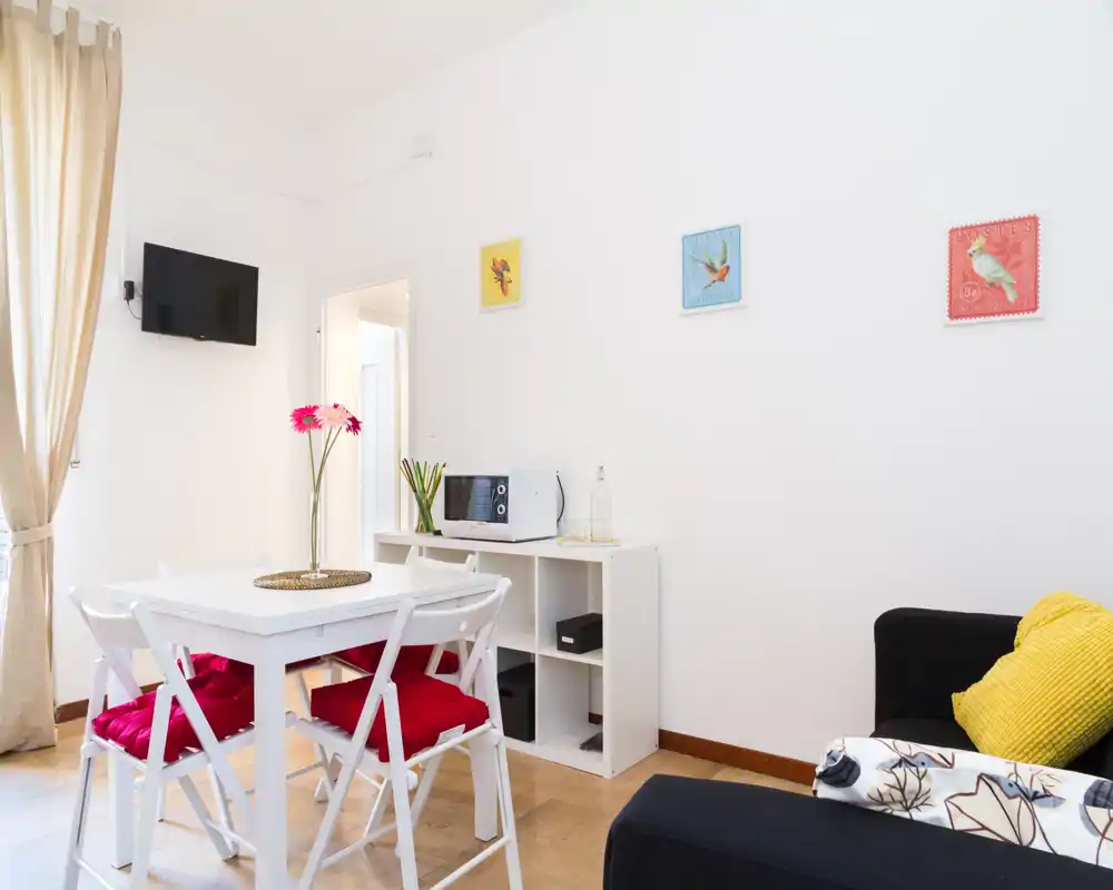 Zona de estar luminosa y bien decorada con mesa de comedor, sillas con cojines rojos y un sofá cómodo — perfecta para estancias urbanas acogedoras.