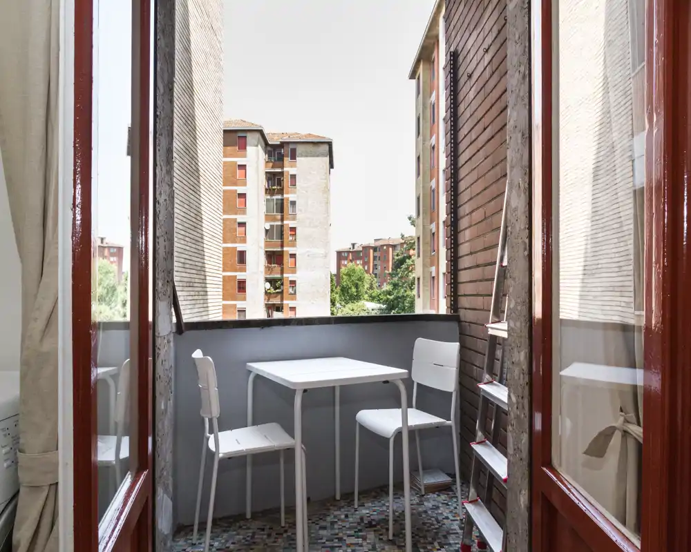 Pequeño balcón amueblado con una mesa compacta y dos sillas, con vistas a edificios residenciales cercanos — rincón luminoso y acogedor para un café.
