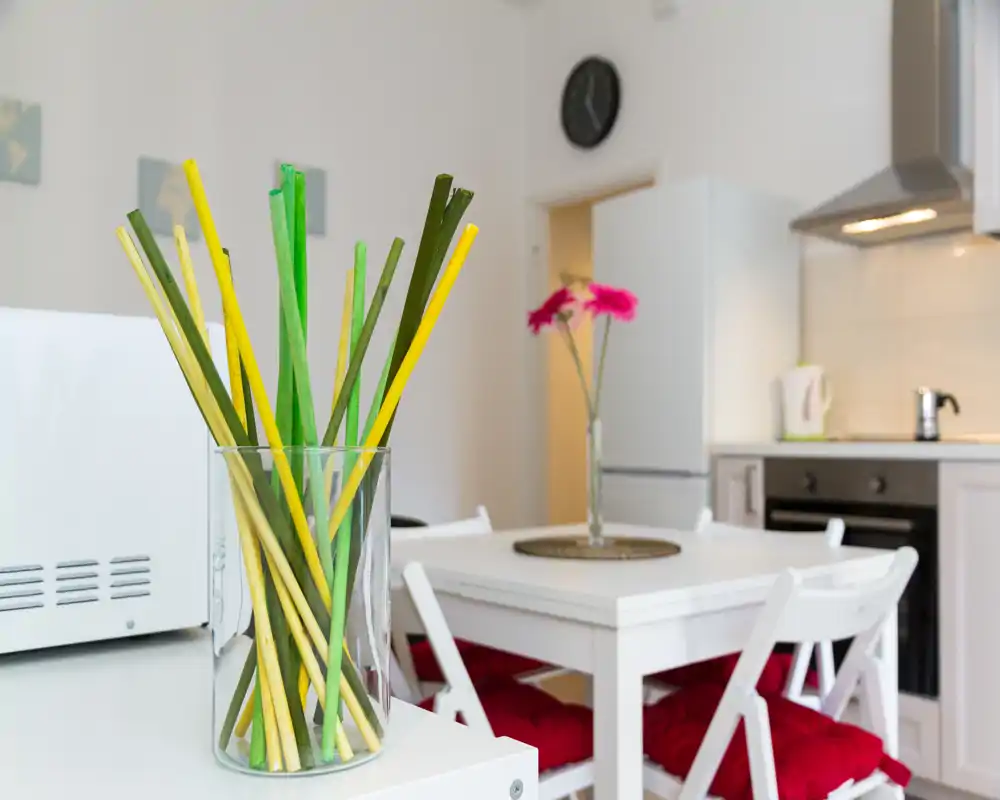 Cocina abierta moderna y luminosa con una mesa blanca pequeña, cojines rojos y jarrones decorativos — ordenada y acogedora para alquileres de corta estancia.