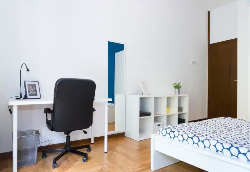 Bright, modern bedroom with a patterned bed, a white desk and an ergonomic chair — ideal for working and resting in the same space.