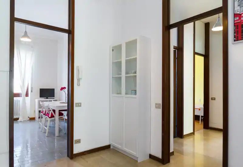 Espace de transition lumineux et propre avec une armoire blanche et une ouverture sur la pièce à vivre/salle à manger. Lumière naturelle, mobilier moderne et agencement soigné parfait pour un appartement compact.