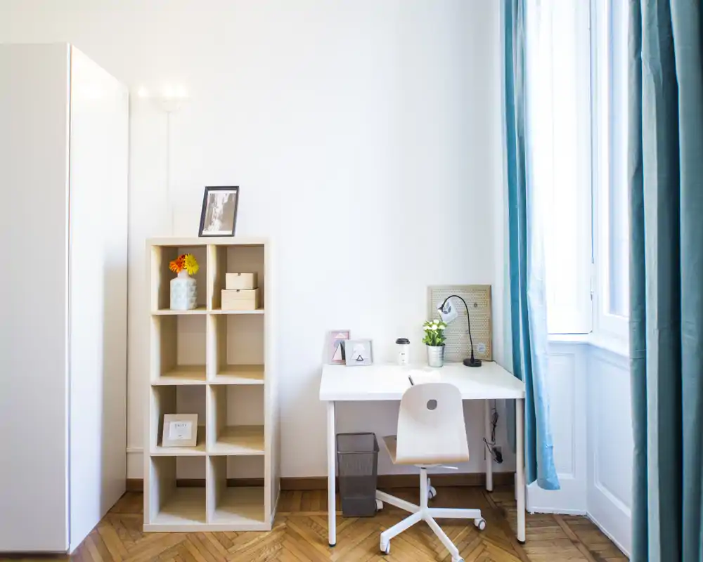 Coin de chambre lumineux et minimaliste avec bureau, étagère et grande fenêtre aux rideaux turquoise — lignes épurées et lumière naturelle, parfait pour étudier ou travailler.