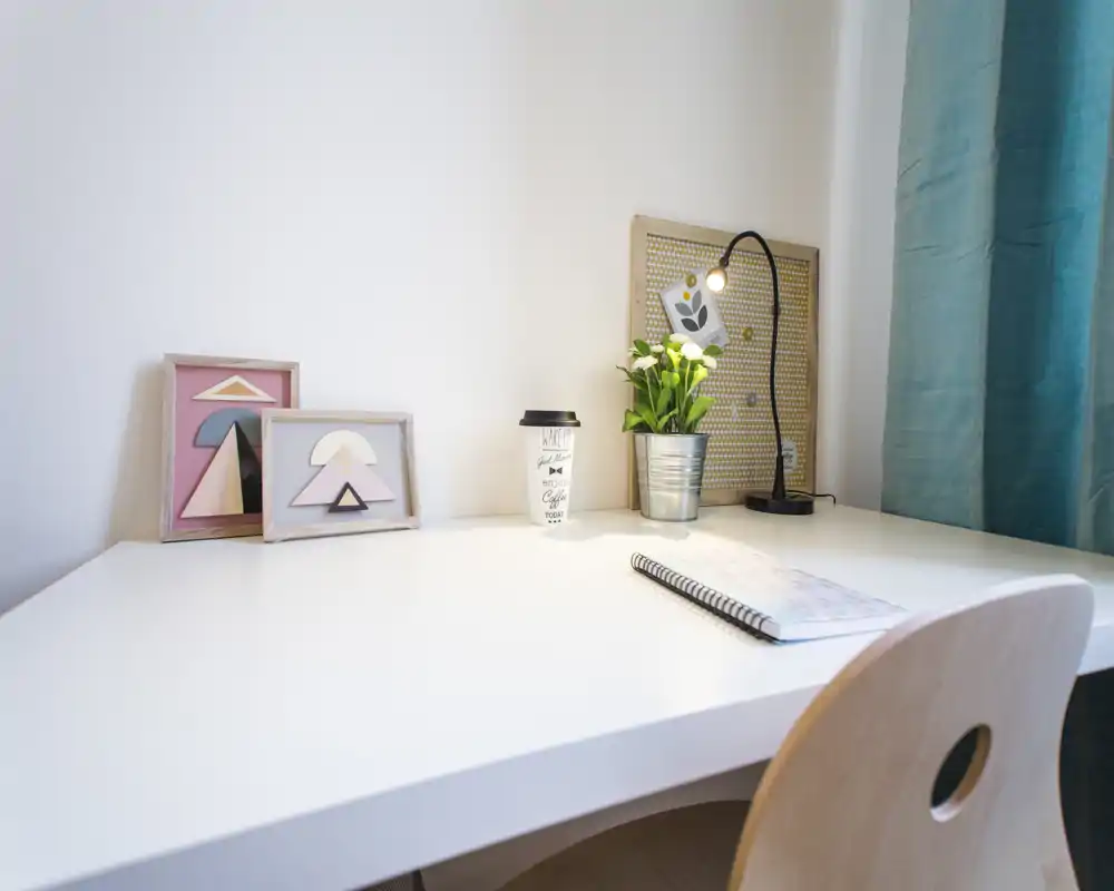 Coin bureau lumineux et soigné avec un bureau blanc, un carnet, une lampe de bureau et une petite plante décorative — parfait pour le travail ou les études.