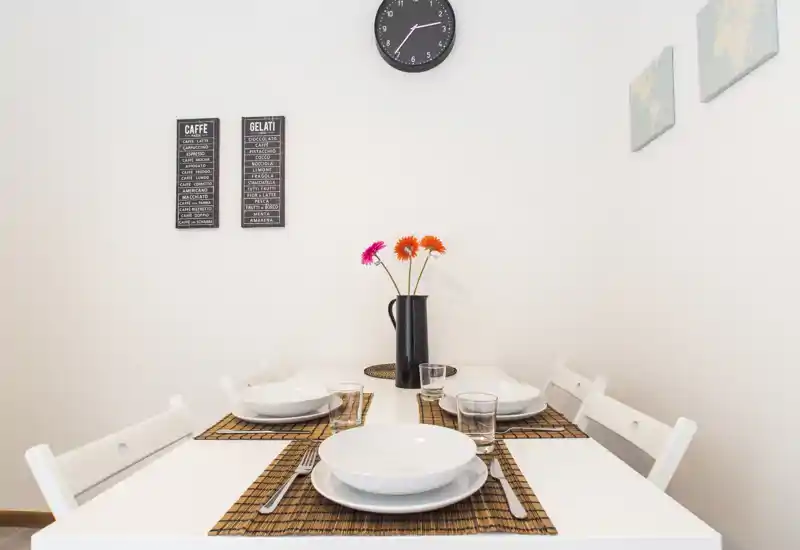 Bright, modern dining area with a neatly set white table for four, decorative placemats and a vase of flowers creating a welcoming atmosphere.